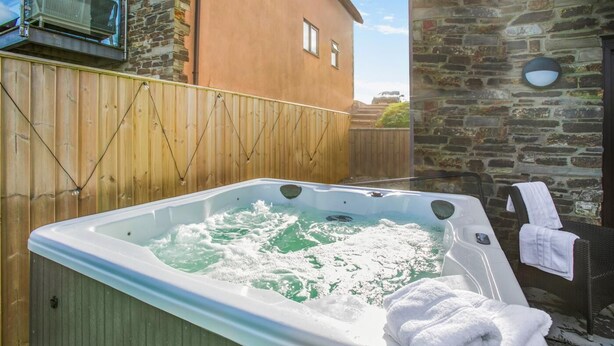 A hot tub with a wooden fence, a stone wall, and a building in the background. - 6 Bed in Winnards Perch (oc-c30624) (Winnard's Perch)