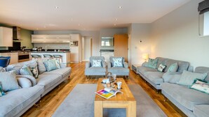 A modern living room with a sofa set, a coffee table, and a kitchen in the background. - 6 Bed in Winnards Perch (oc-c30624) (Winnard's Perch)