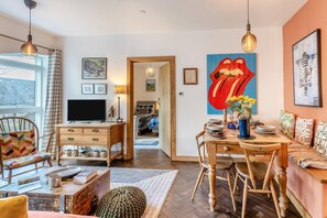 Ein gemütliches Wohnzimmer mit Fernseher, Holzmöbeln, einem Essbereich mit Tisch und Stühlen sowie einem farbenfrohen Kunstwerk mit Lippenmotiven.