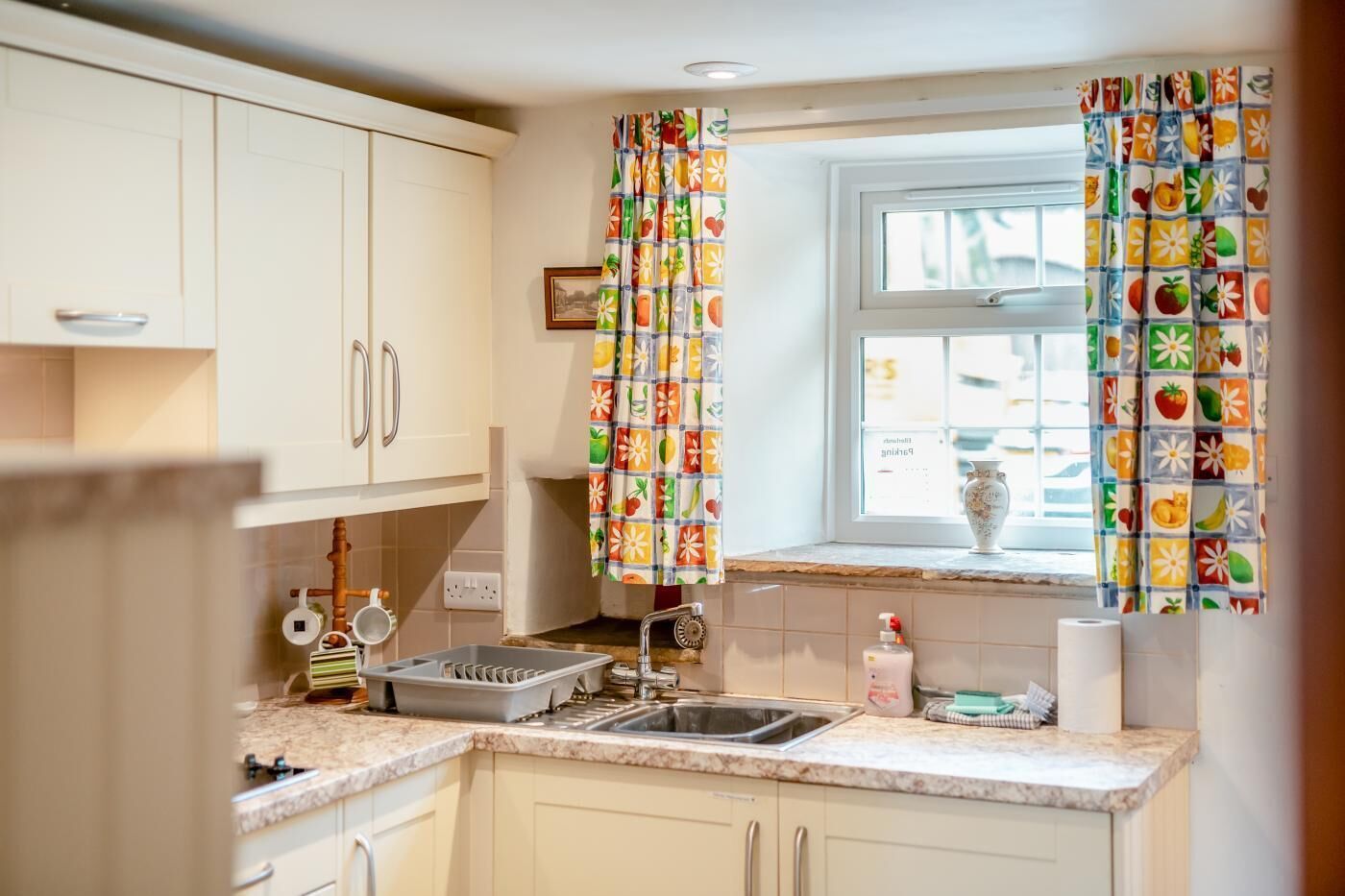 A kitchen with white cabinets, a sink, and a window with fruit-patterned curtains.