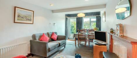 Una sala de estar con sofá, un sillón rojo, una mesa de comedor con sillas, televisor y chimenea.