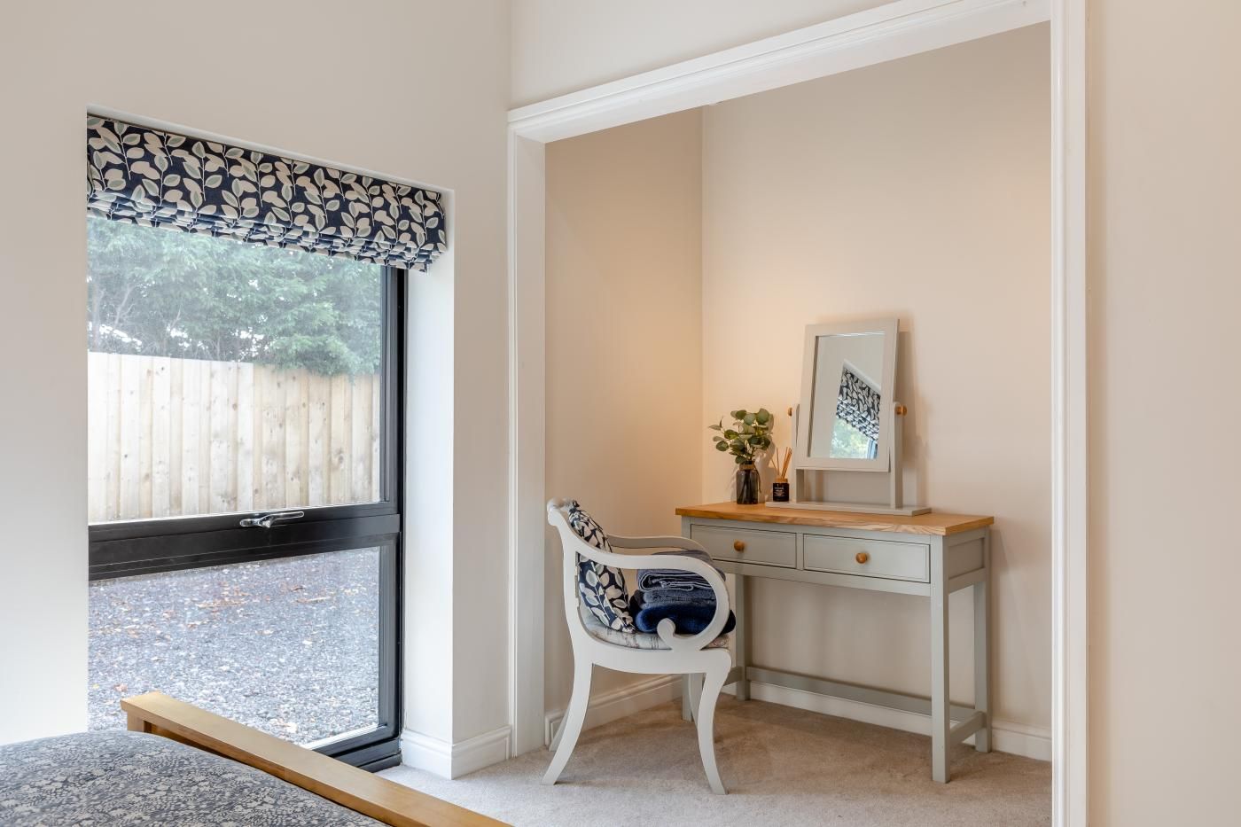 Une pièce comprenant un bureau, une chaise, une fenêtre avec des stores et donnant sur une clôture en bois.