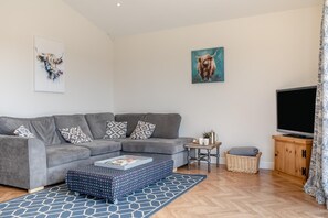 A modern living room with a grey sectional sofa, a patterned ottoman, a coffee table, a television, and a wicker basket. - 2 Bed in Stanton (oc-p30248) (Ticknall)