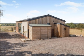 A single-story building with a sloped roof, a fenced area, and a gravel driveway.