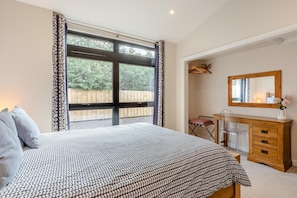 A bedroom with a large bed, a wooden dresser, a mirror, and a window with curtains.