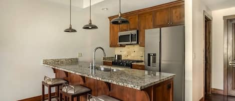 Una cocina con encimera de granito, electrodomésticos de acero inoxidable, armarios de madera e iluminación colgante.
