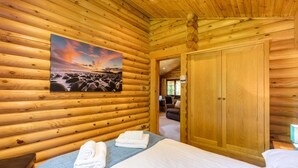 A log cabin room with a bed, towels, a painting of a beach, and a wooden wardrobe. - 2 Bed in Felton (oc-c30643) (Thirston)