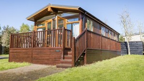 Una cabaña de troncos moderna con terraza de madera, ventanas grandes y una escalera que conduce a la entrada.