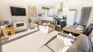 Una sala de estar moderna con chimenea, un televisor de pantalla plana y un comedor con una mesa dispuesta para cuatro.