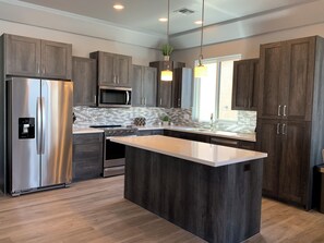 A modern kitchen with dark wood cabinets, stainless steel appliances, a central island, and pendant lighting. - Gorgeous Pool and RV Garage Home! (Lake Havasu City)