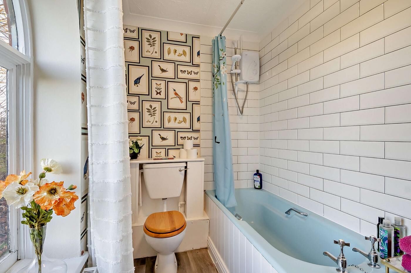 Et badeværelse med toilet, bruser og en væg med hvide fliser samt indrammede billeder.
