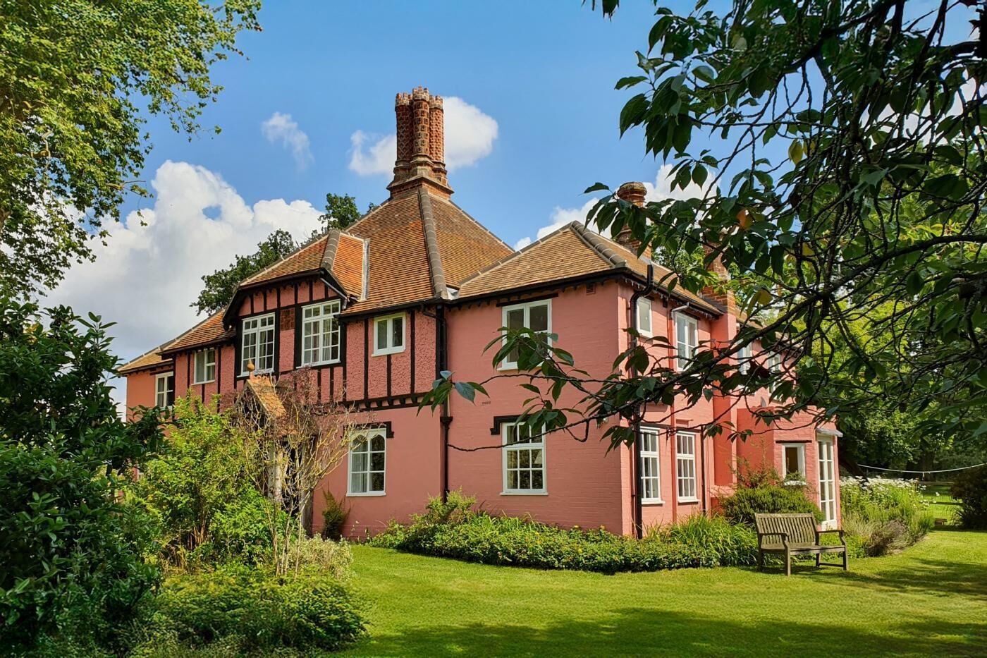 Ein traditionelles Haus im Tudor-Stil mit roter Fassade, mehreren Schornsteinen und einem gepflegten Garten mit Bank.