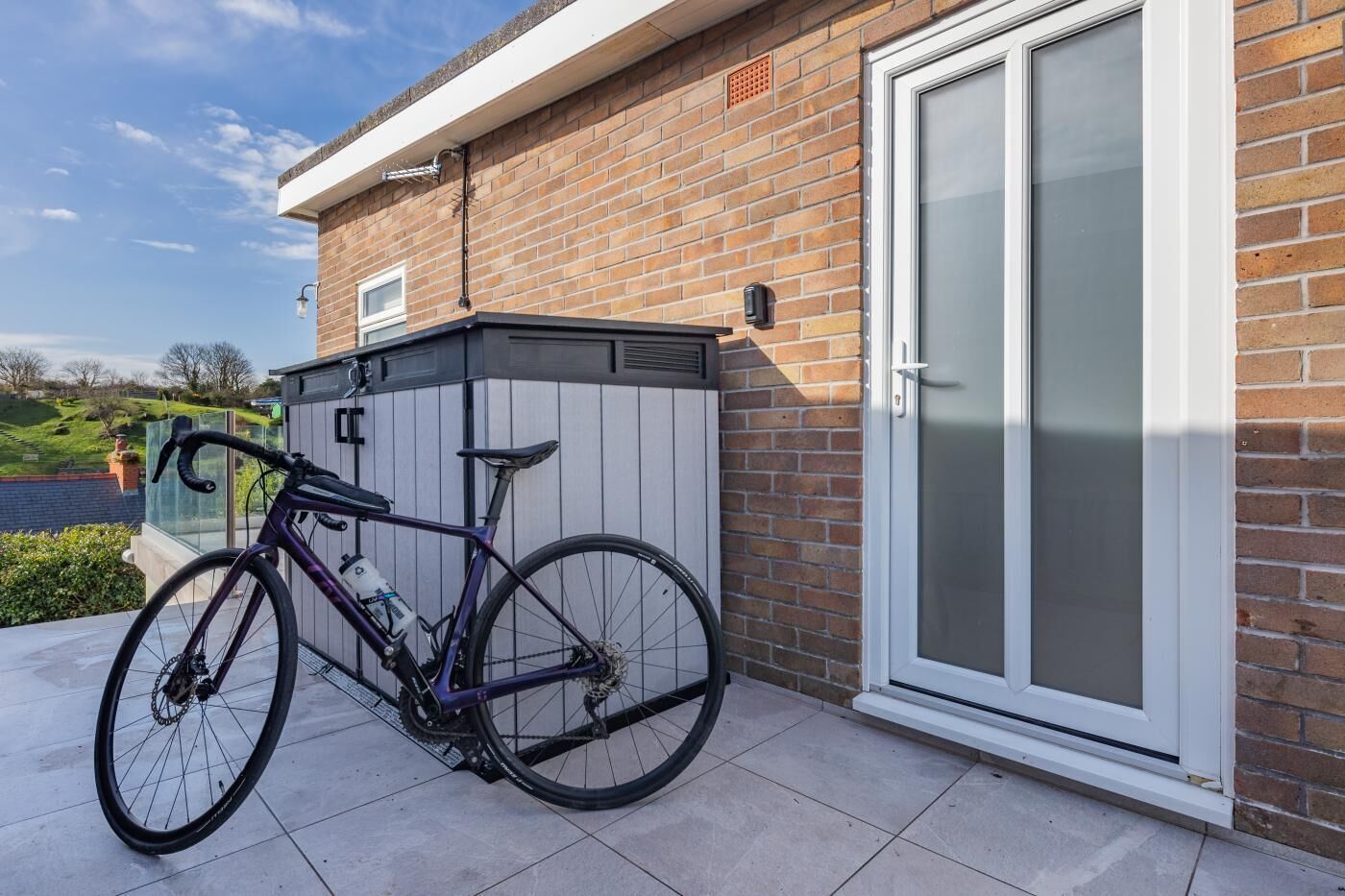 Een fiets geparkeerd voor een huis met een gevel van baksteen en een schuifdeur met glas.