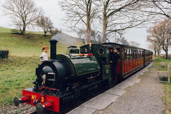 A vintage steam train with a black and red exterior, a conductor, and a passenger car.