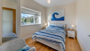 A bedroom with a bed, a chair, a bedside table, a lamp, a window, and a painting.