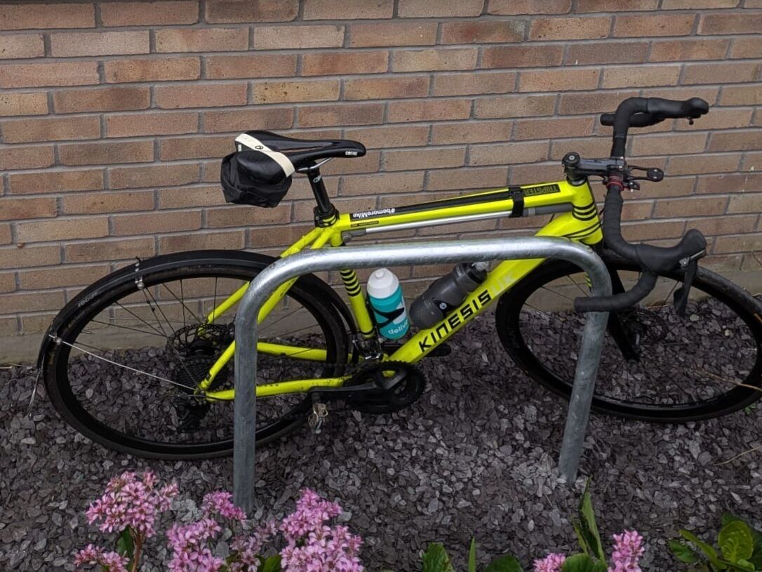 A yellow bicycle with the brand name 'Kinesis' parked against a brick wall.