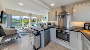 A modern kitchen with a central island, stainless steel appliances, and a view of the outdoors.