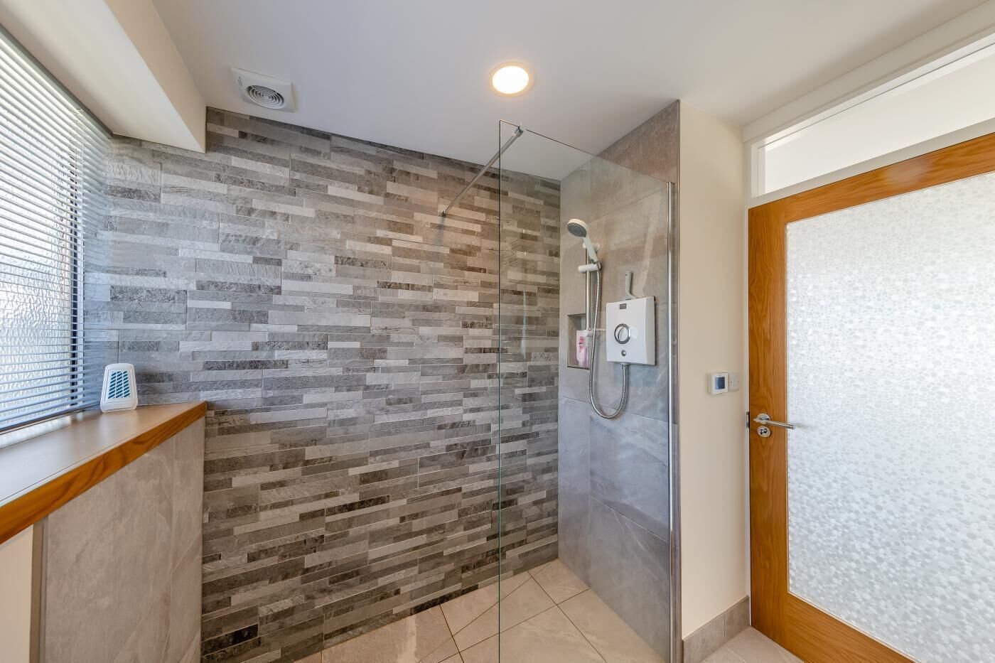 A modern bathroom with a glass shower enclosure, a tiled wall, and a wooden vanity.