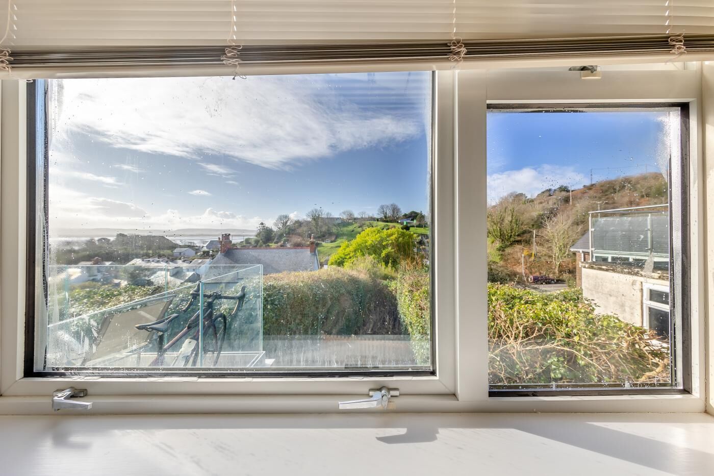A large window with a view of a coastal landscape, including a grassy area and a building with a sloped roof.