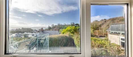 A large window with a view of a coastal landscape, including a grassy area and a building with a sloped roof.