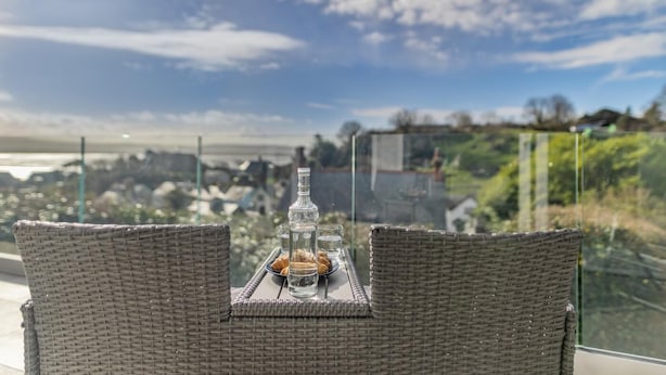 A wicker chair with a tray table set with a bottle, glasses, and pastries.