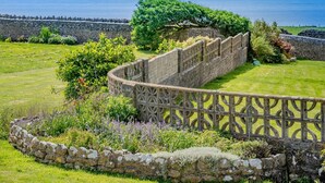 Un mur de pierre agrémenté d’une clôture décorative, une végétation luxuriante et une vue sur la mer.