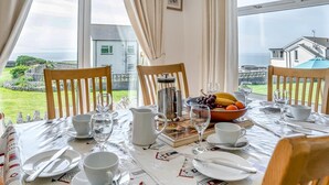 Une table à manger dressée pour quatre personnes, avec vue sur la mer et un jardin.