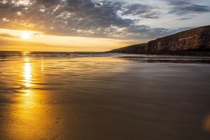 A beach with a sunset, calm waves, and a rocky cliff. - 3 Bed in Southerndown (oc-l10852) (Southerndown)