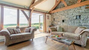 Ein geräumiges Wohnzimmer mit zwei gemusterten Sofas, einem Couchtisch mit Zeitschriften und Früchten sowie einer Steinwand.