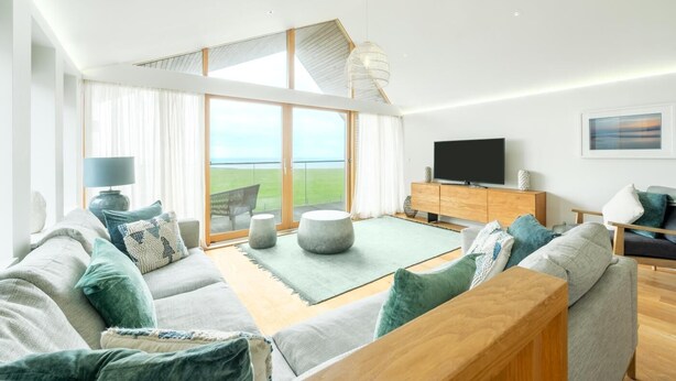 Un salon moderne avec un canapé, un pouf et un téléviseur à écran plat.