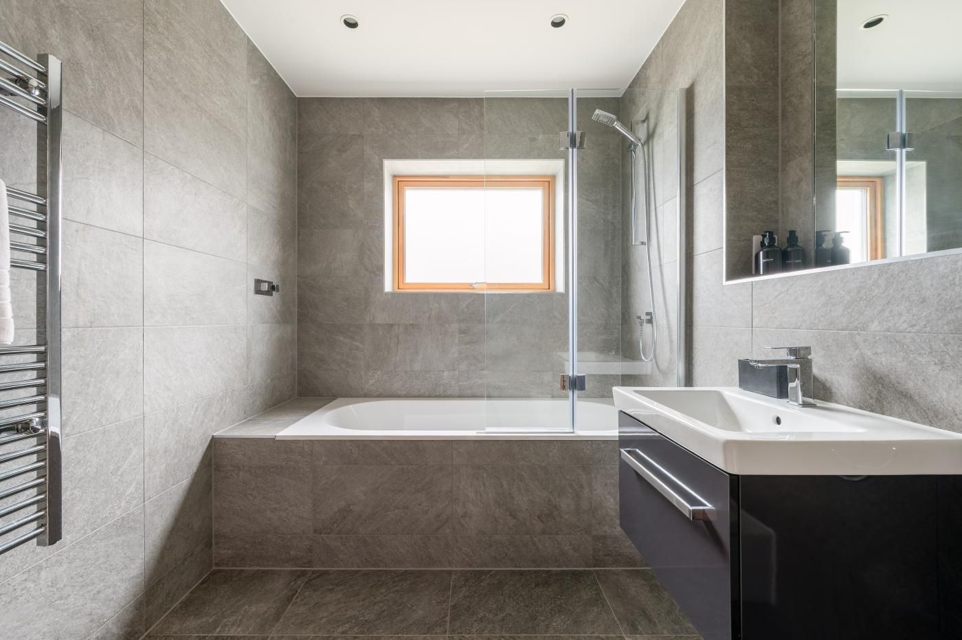 Ein modernes Badezimmer mit einer gläsernen Duschkabine, einer großzügigen Badewanne und einem Waschtisch mit Spiegel.