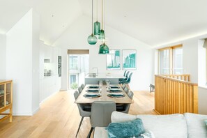 A spacious dining area with a long table set for four, a kitchen in the background, and a view of the outdoors. - 3 Bed in St. Eval (oc-k30666) (Saint Eval)