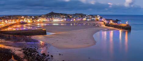 Une ville côtière au crépuscule, avec une plage, une promenade et des bâtiments le long du front de mer.