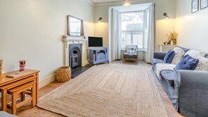 A cozy living room with a fireplace, a sofa, a TV, and a large window. - 3 Bed in St. Ives (oc-s30653) (Saint Ive)