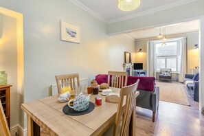 A cozy dining area with a wooden table set for breakfast, a fireplace, and a comfortable seating area with a sofa and armchairs. - 3 Bed in St. Ives (oc-s30653) (Saint Ive)