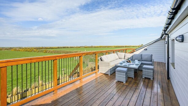 Un terrazza in legno con mobili da esterno, una ringhiera e vista su un prato verde.