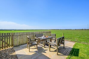 An outdoor patio with a table and chairs, surrounded by a wooden fence, overlooking a green field. - 3 Bed in St. Mawgan (oc-h30677) (Saint Eval)