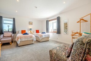 A hotel room with two beds, a sofa, a chair, and a wooden hanger rack. - 3 Bed in St. Mawgan (oc-h30677) (Saint Eval)