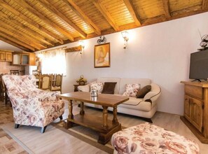 Ein gemütliches Wohnzimmer mit Holzboden, einer Couch, einem floralen Sessel, einem Couchtisch und einem Fernseher auf einer Holzkommode.