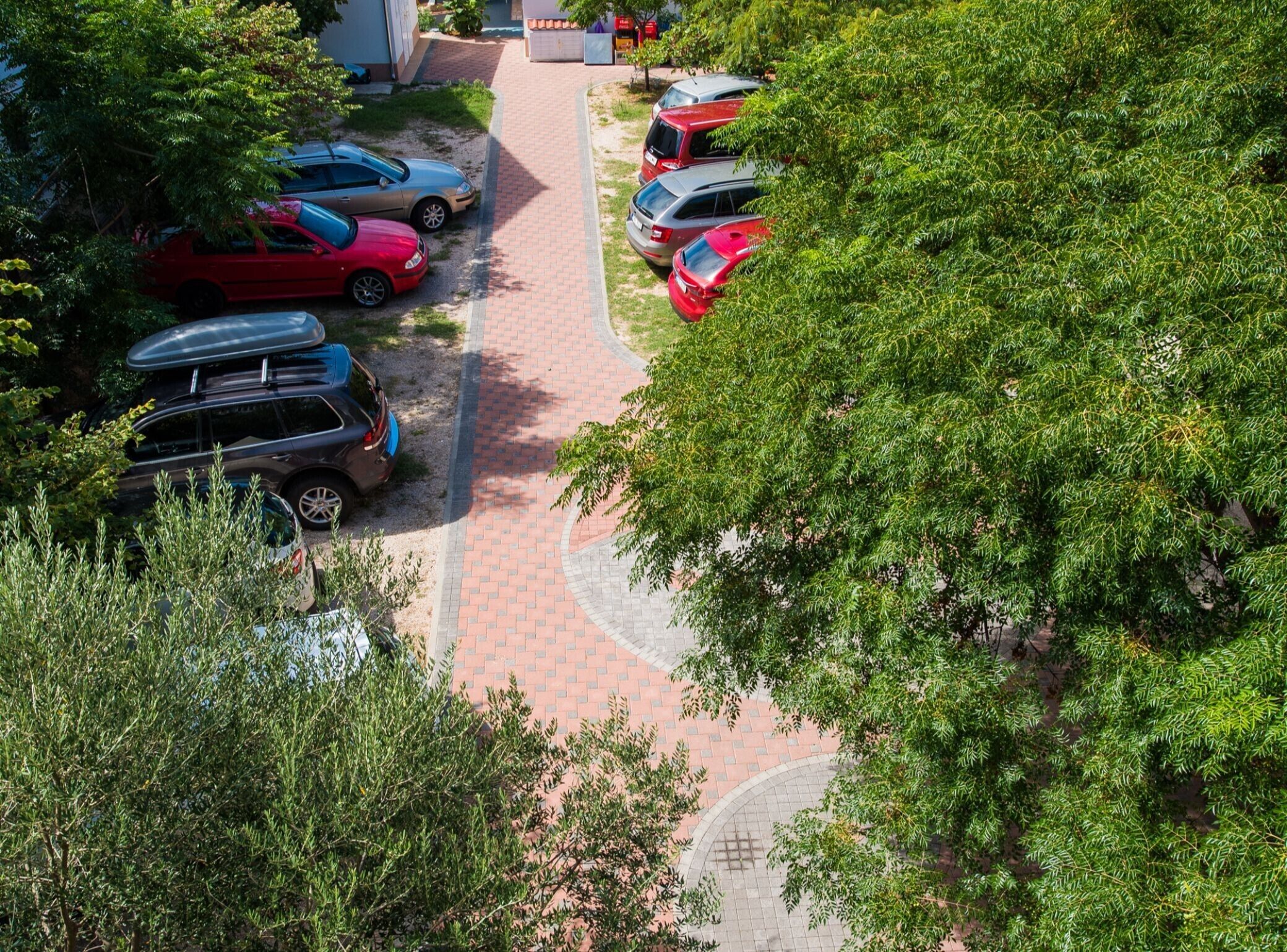 A parking area with multiple cars and a brick pathway.