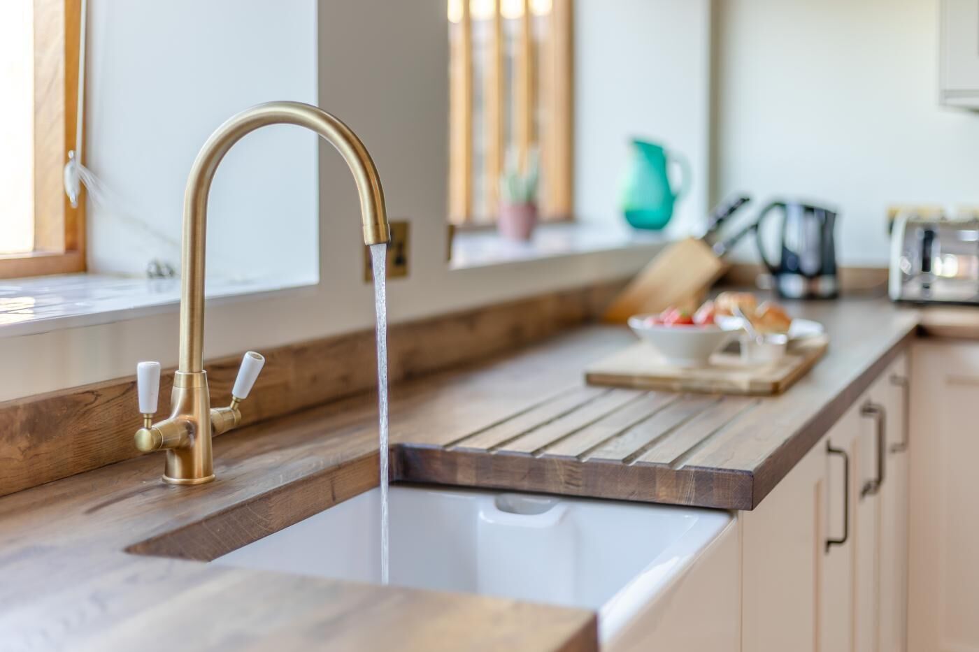 A kitchen with a modern faucet, wooden countertop, and a window with blinds.