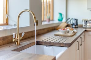 Une cuisine dotée d’un robinet moderne, d’un plan de travail en bois et d’une fenêtre avec des stores.