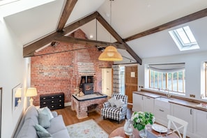 Un espace de vie de style loft avec des poutres en bois apparentes, une cheminée en briques, un coin repas et une cuisine dotée d’une grande fenêtre.