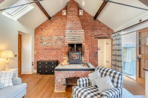 A loft-style room with a brick fireplace, a sofa, a dresser, and a skylight. - 2 Bed in Llangedwyn (oc-l30530) (Llangedwyn)