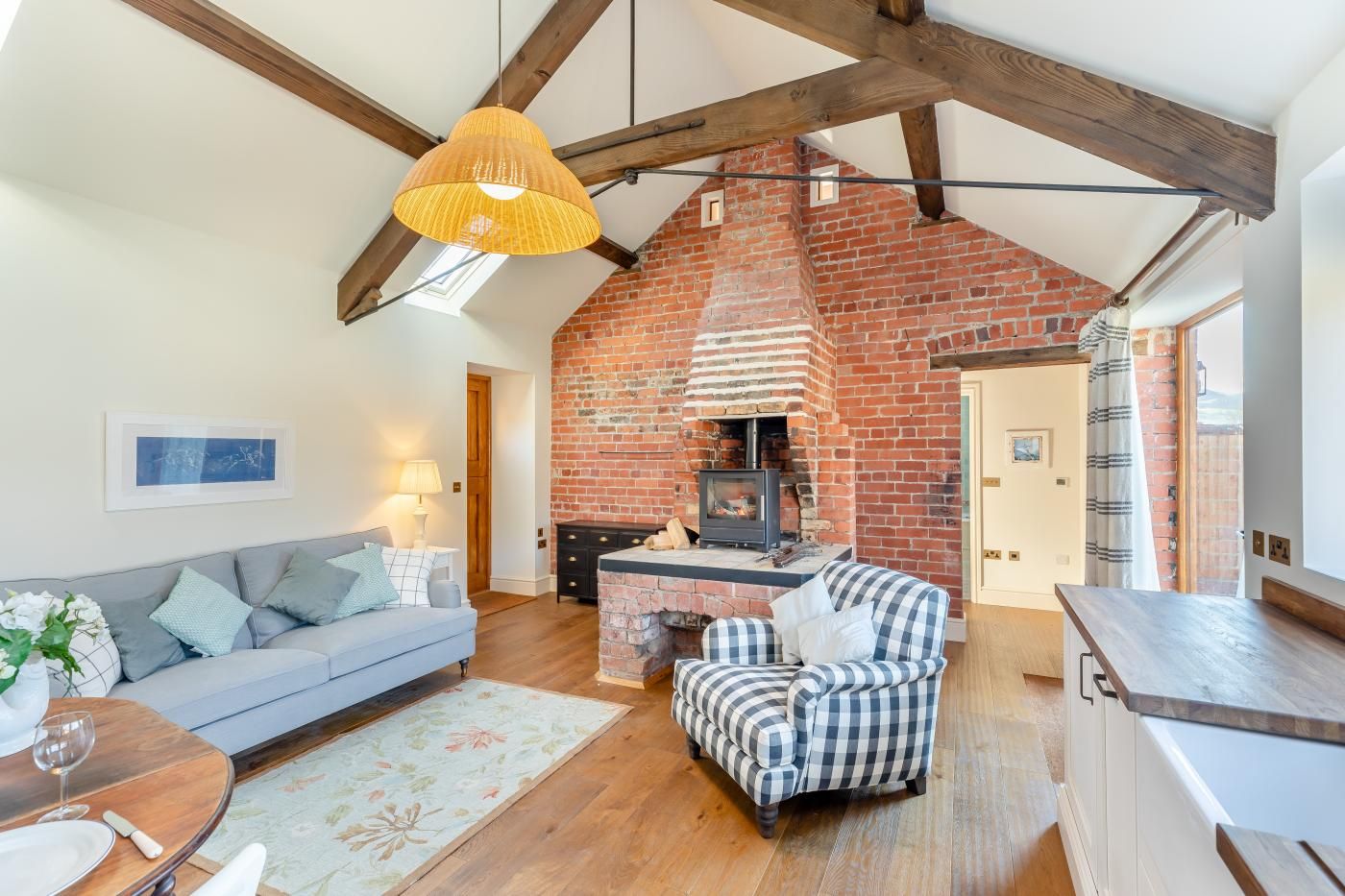 A cozy living room with a sofa, a checkered armchair, a wooden dining table, and a brick fireplace.