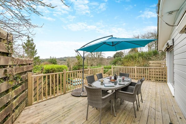 A wooden deck with a round table and chairs, a blue umbrella, and a view of the countryside. - 2 Bed in Mawgan (oc-c30671) (Mawgan)