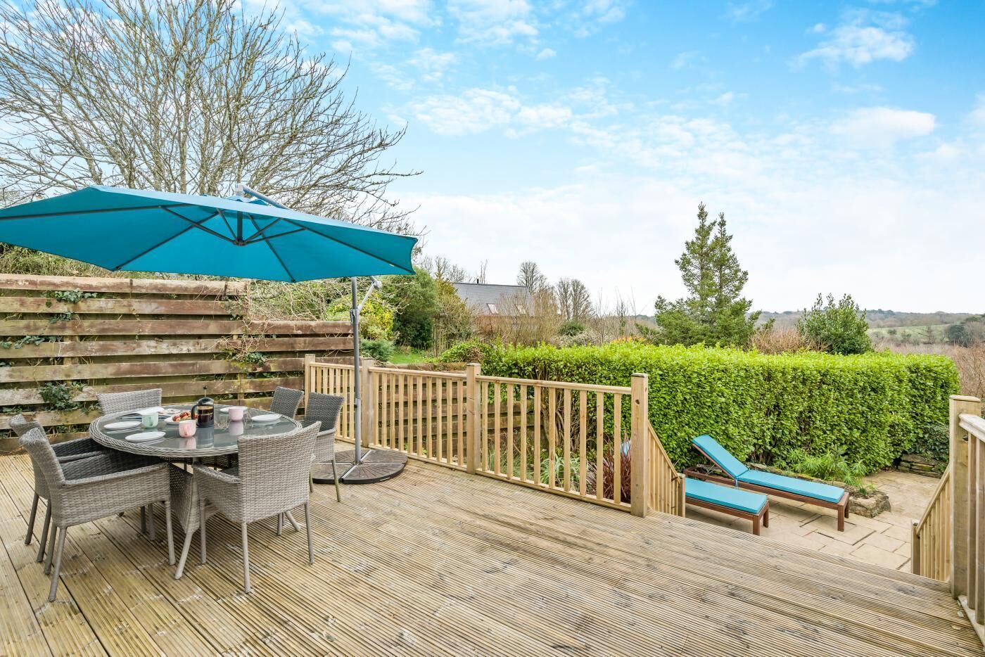 A wooden deck with a round table and chairs, a blue umbrella, and a lounge chair.