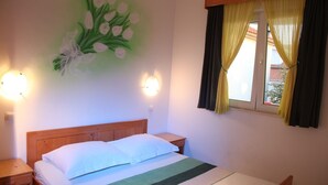 A bedroom with a wooden bed, a nightstand, a wall-mounted light, and a window with yellow curtains. - Apartments Gabi - Two Bedroom/Balcony/SeaView (A3) (Srima)