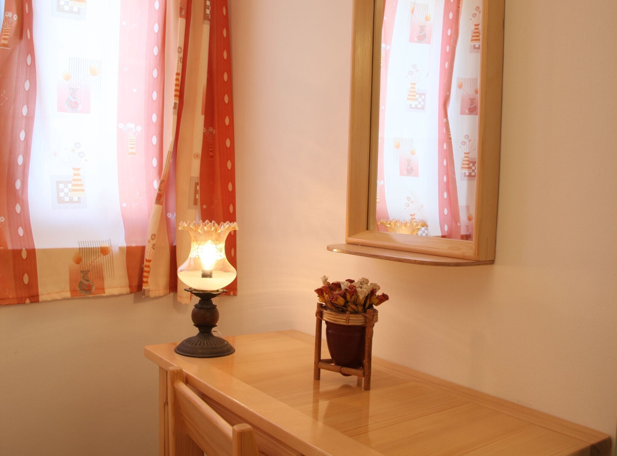 Een houten tafel met een brandende tafellamp, een kleine potplant en een spiegel aan de muur.