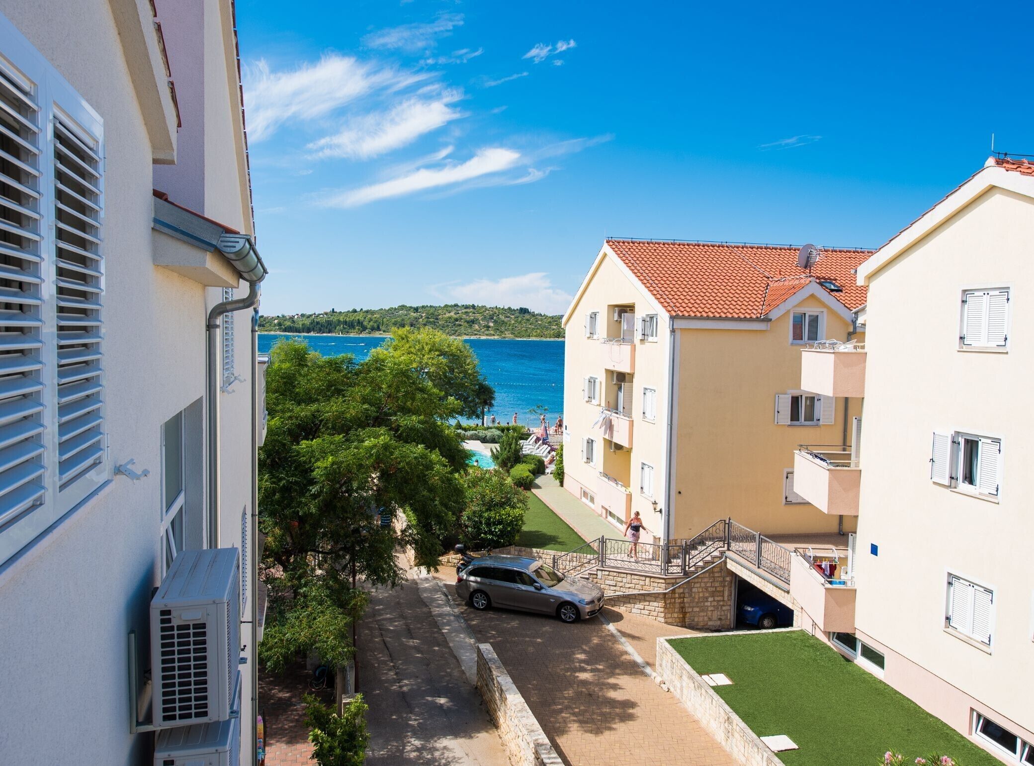 A coastal residential area with a clear view of the sea, a paved street, and a parked car.